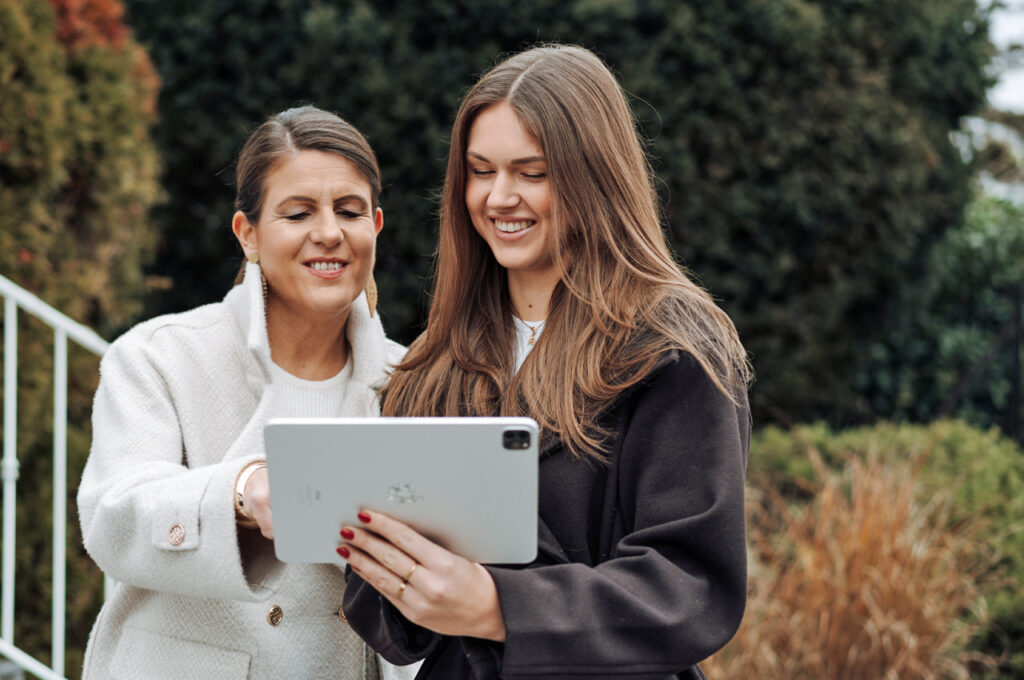 Zwei Deutsche Frauen mit dunklem Haar arbeiten am Tablet mobil draußen im Garten mit CadiaOffice